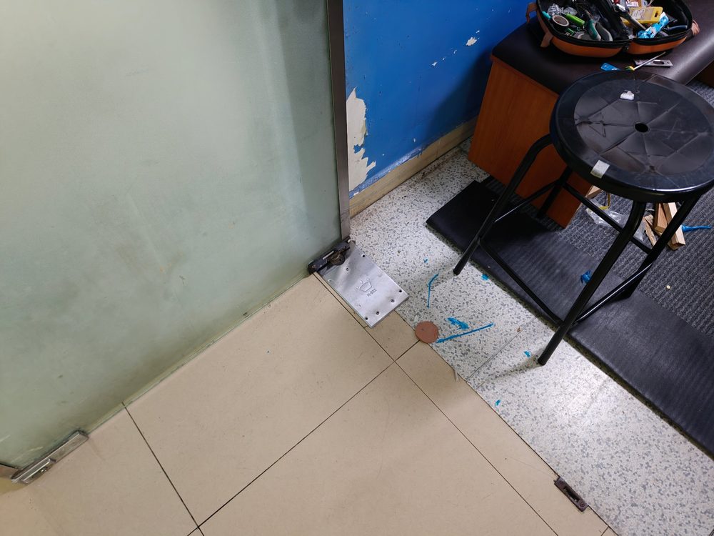 玻璃门下方施工现场，地弹簧底座已嵌入地面，地砖开孔完成找平
